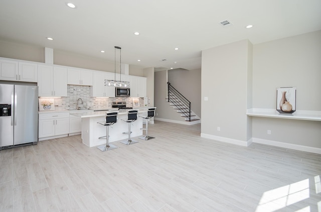 kitchen featuring a center island, sink, appliances with stainless steel finishes, decorative light fixtures, and white cabinetry