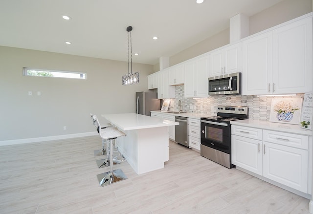 kitchen featuring a kitchen island, white cabinetry, stainless steel appliances, and hanging light fixtures