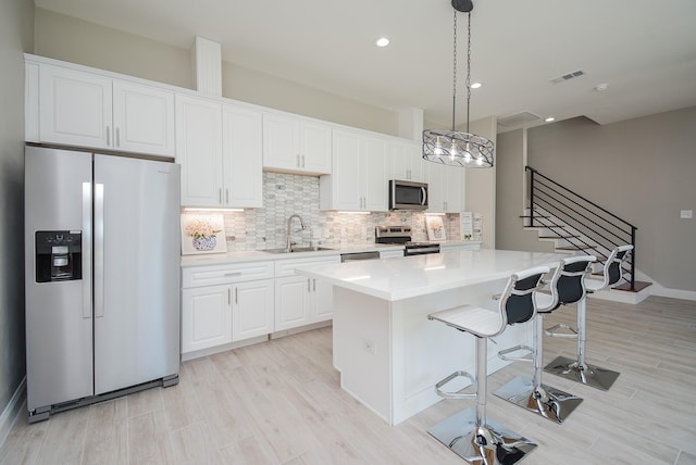 kitchen with a center island, sink, appliances with stainless steel finishes, decorative light fixtures, and white cabinetry