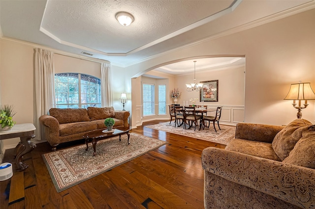 living room with a textured ceiling, a raised ceiling, crown molding, wood-type flooring, and a chandelier