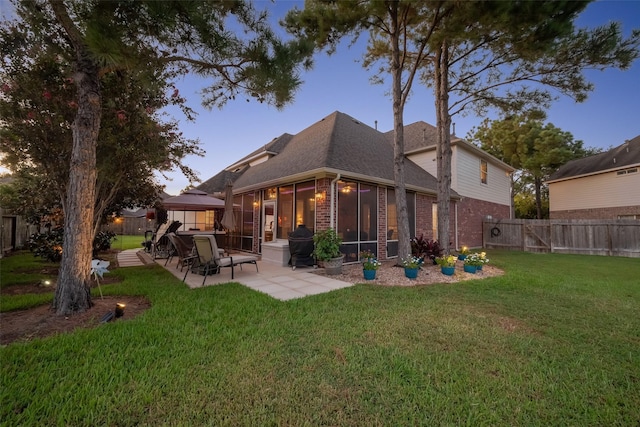 back house at dusk featuring a gazebo, a sunroom, a yard, and a patio