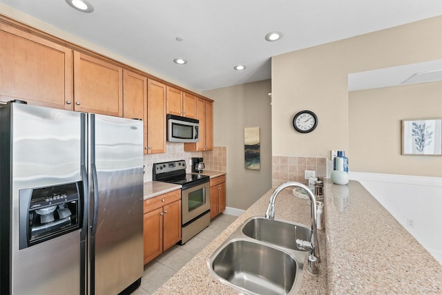 kitchen featuring light stone countertops, appliances with stainless steel finishes, backsplash, sink, and light tile patterned floors