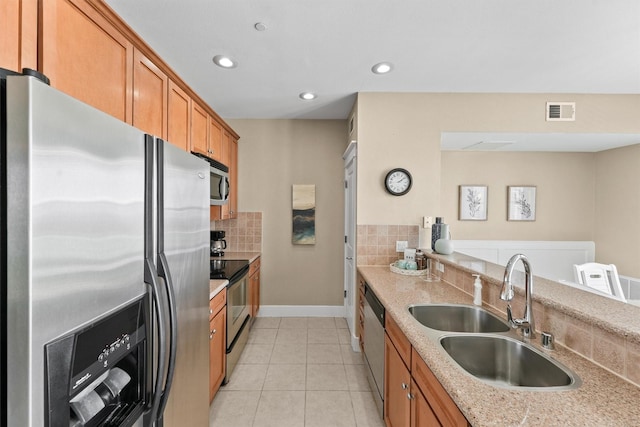 kitchen with light stone countertops, appliances with stainless steel finishes, backsplash, sink, and light tile patterned floors