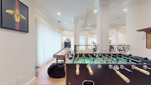 game room with light wood-type flooring, crown molding, and decorative columns