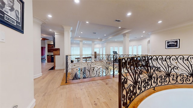 corridor featuring decorative columns, a raised ceiling, crown molding, and light hardwood / wood-style flooring