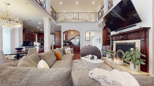 living room with a high end fireplace, a towering ceiling, ornate columns, hardwood / wood-style flooring, and an inviting chandelier