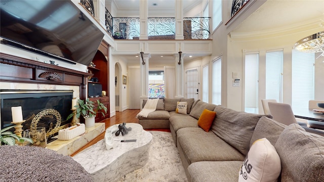 living room featuring wood-type flooring, a premium fireplace, crown molding, and a towering ceiling