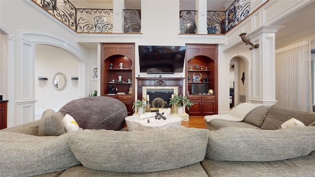 living room featuring built in shelves, a high ceiling, decorative columns, hardwood / wood-style flooring, and ornamental molding