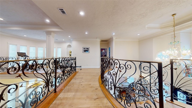 hall with ornate columns, a notable chandelier, light wood-type flooring, a textured ceiling, and ornamental molding