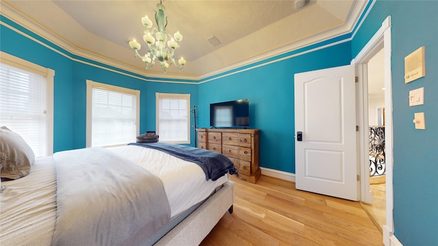 bedroom with a raised ceiling, light hardwood / wood-style flooring, and a chandelier