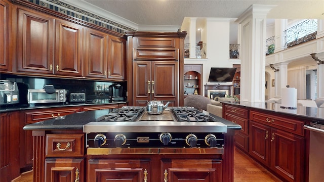 kitchen featuring stainless steel appliances, ornamental molding, dark stone counters, a kitchen island, and hardwood / wood-style flooring