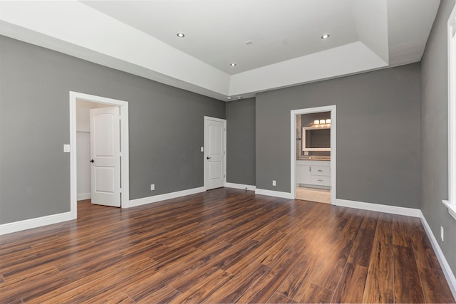 unfurnished bedroom featuring ensuite bathroom, dark wood-type flooring, and a tray ceiling