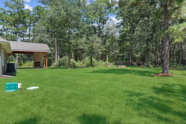 view of yard featuring an outdoor fireplace and central AC