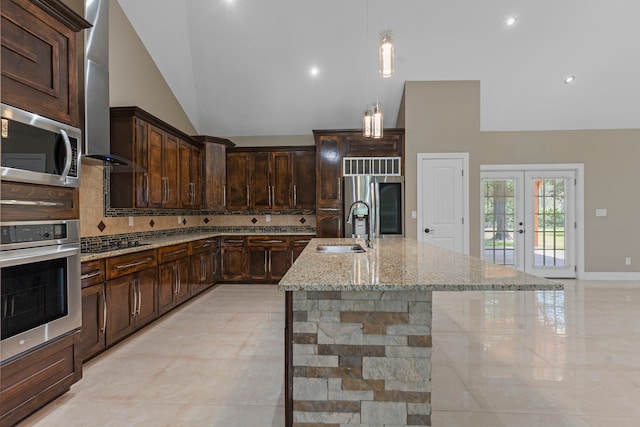 kitchen with a center island with sink, decorative backsplash, sink, light stone countertops, and stainless steel appliances