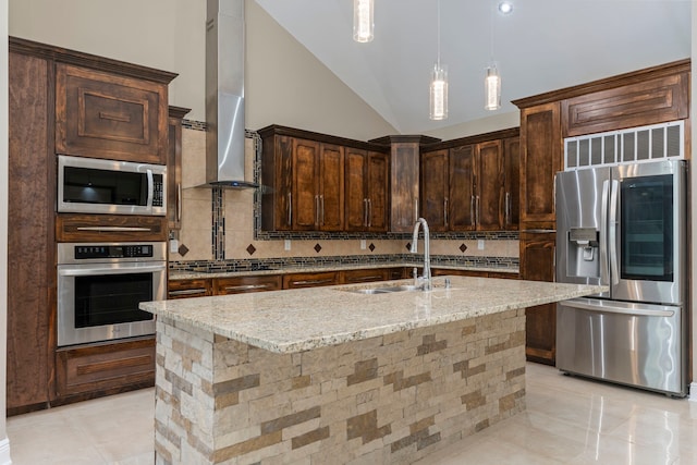 kitchen with light stone countertops, extractor fan, stainless steel appliances, sink, and a kitchen island with sink