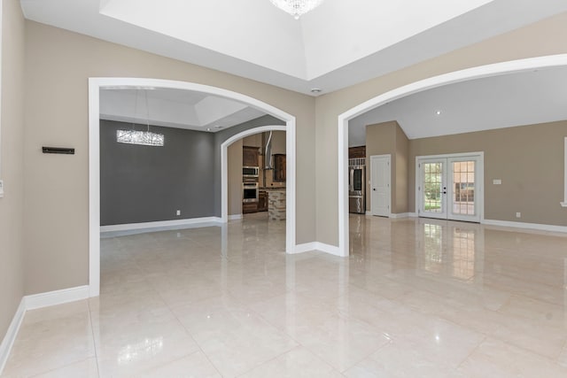 empty room with a chandelier, a tray ceiling, and french doors