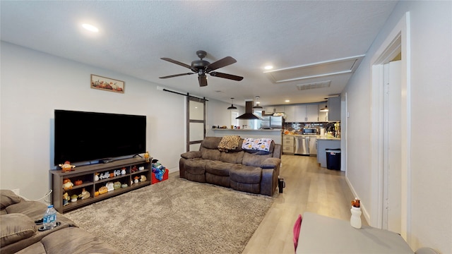 living room with a barn door, ceiling fan, light hardwood / wood-style floors, and a textured ceiling