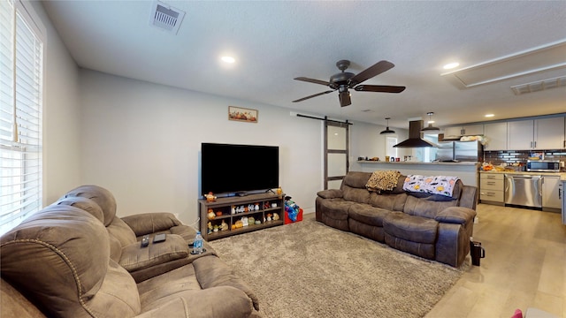 living room with a barn door, ceiling fan, and light hardwood / wood-style floors