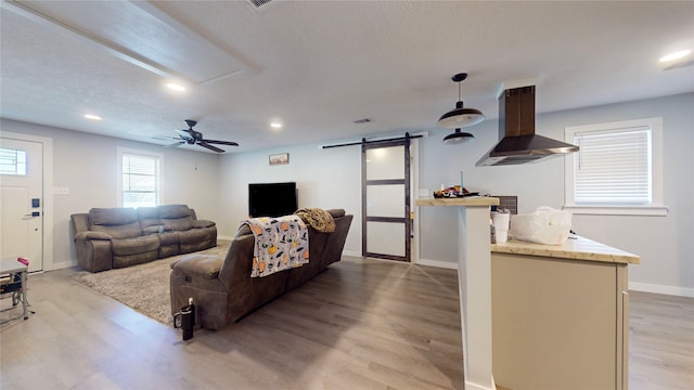 living room featuring a textured ceiling, a barn door, light hardwood / wood-style floors, and ceiling fan