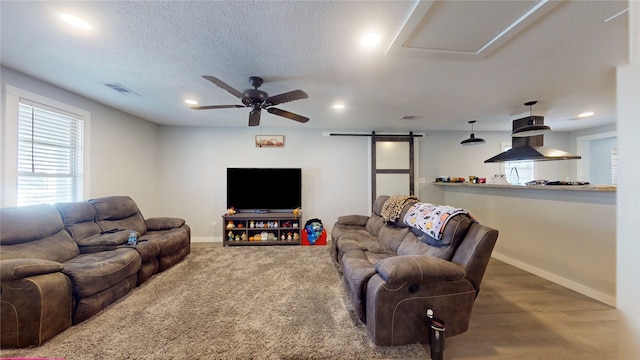 living room with a barn door, ceiling fan, and a textured ceiling