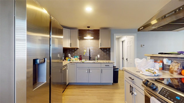 kitchen with wall chimney range hood, hanging light fixtures, sink, appliances with stainless steel finishes, and light stone counters