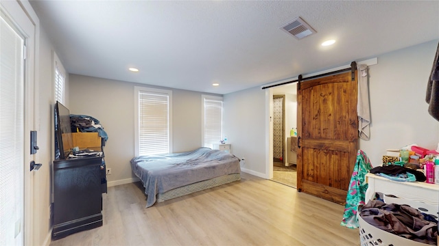 bedroom with a barn door and light hardwood / wood-style floors