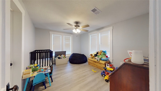 bedroom featuring a crib, a textured ceiling, light hardwood / wood-style flooring, and ceiling fan