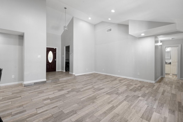 unfurnished living room featuring light hardwood / wood-style floors, high vaulted ceiling, and a notable chandelier