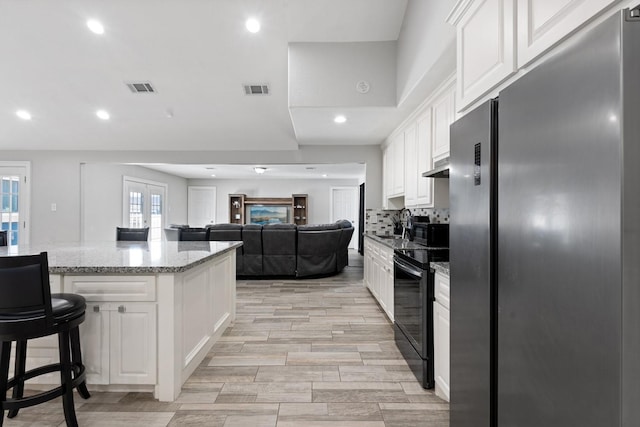 kitchen with a breakfast bar, black electric range, light stone counters, white cabinetry, and stainless steel refrigerator