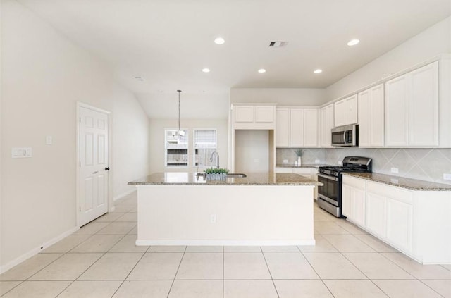 kitchen with light stone countertops, appliances with stainless steel finishes, sink, white cabinets, and an island with sink