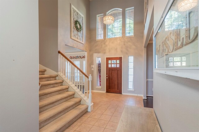 tiled entrance foyer with an inviting chandelier, a towering ceiling, and a healthy amount of sunlight