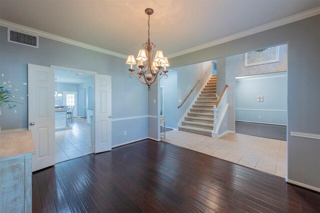 empty room featuring wood-type flooring, ornamental molding, and a notable chandelier