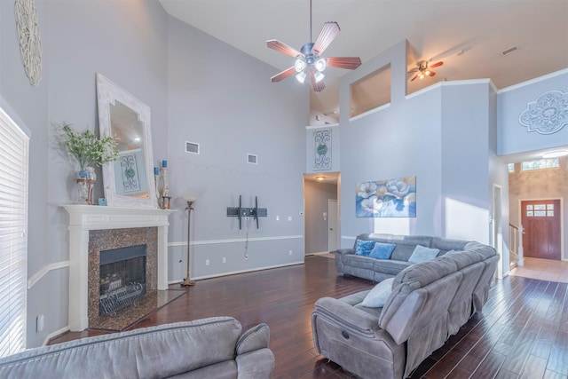 living room featuring a premium fireplace, ceiling fan, dark hardwood / wood-style floors, a high ceiling, and ornamental molding