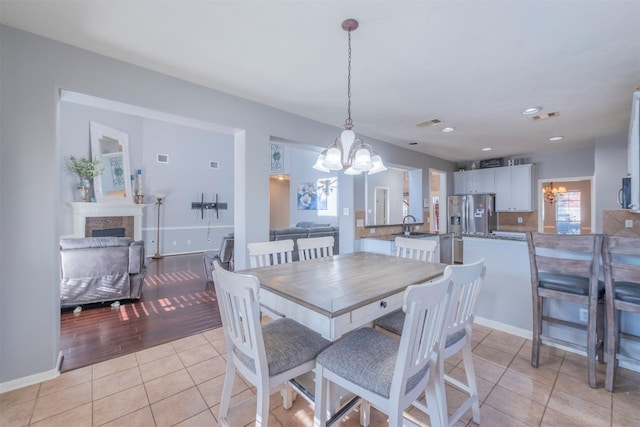 dining area featuring an inviting chandelier, light tile patterned flooring, sink, and a tile fireplace