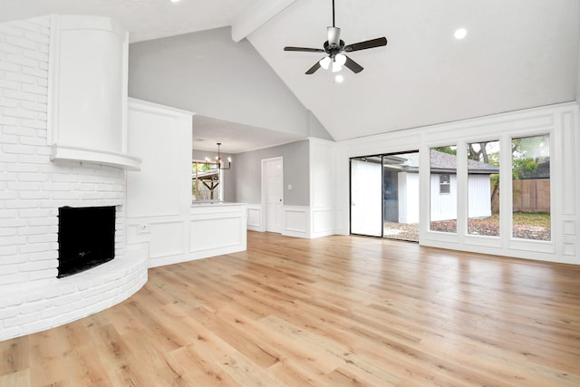 unfurnished living room with beam ceiling, high vaulted ceiling, light hardwood / wood-style floors, a fireplace, and ceiling fan with notable chandelier