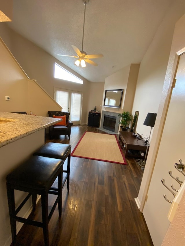 dining area with ceiling fan, dark hardwood / wood-style flooring, a textured ceiling, vaulted ceiling, and a tiled fireplace