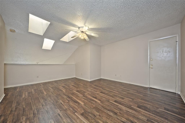 additional living space with a textured ceiling, dark hardwood / wood-style floors, ceiling fan, and vaulted ceiling with skylight