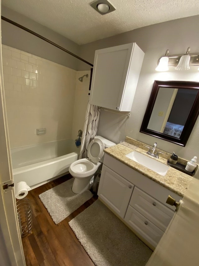 full bathroom with vanity, hardwood / wood-style flooring, tiled shower / bath combo, toilet, and a textured ceiling