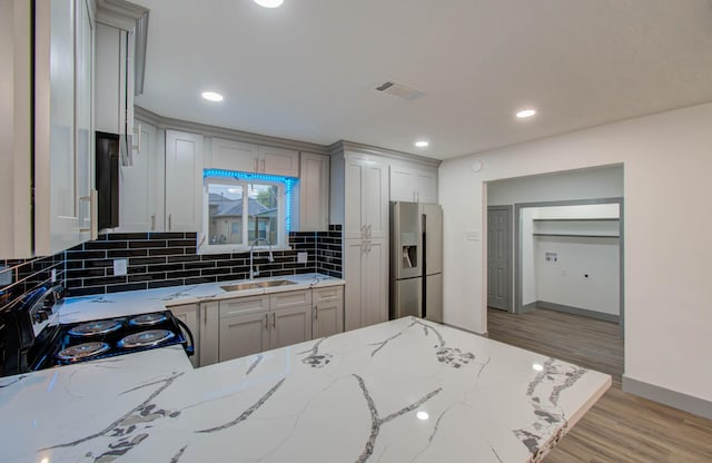 kitchen featuring light stone countertops, electric stove, tasteful backsplash, stainless steel refrigerator with ice dispenser, and sink