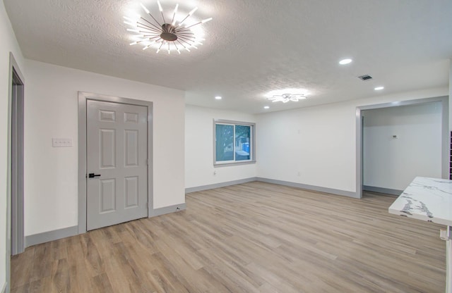 empty room with a textured ceiling and light hardwood / wood-style flooring