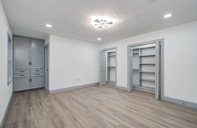 unfurnished bedroom with a textured ceiling, light hardwood / wood-style floors, and two closets