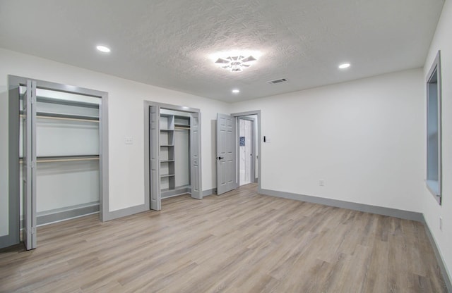 unfurnished bedroom featuring a textured ceiling, two closets, and light wood-type flooring