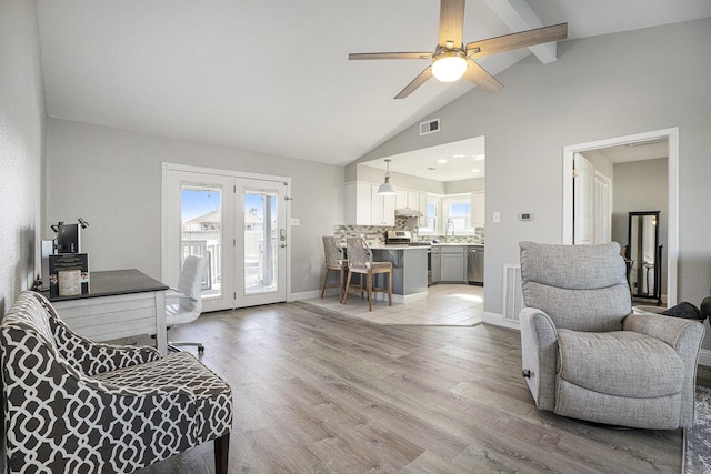 living room with a wealth of natural light, light hardwood / wood-style flooring, ceiling fan, and lofted ceiling with beams