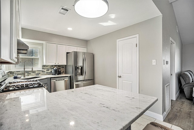 kitchen featuring white cabinets, decorative backsplash, light stone counters, kitchen peninsula, and stainless steel appliances