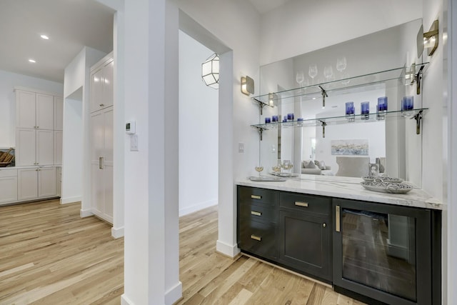 bar with wine cooler, light stone countertops, light hardwood / wood-style flooring, and white cabinets