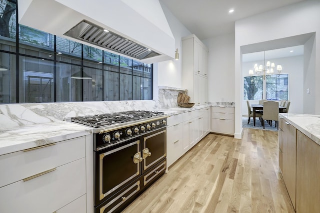 kitchen with light stone countertops, double oven range, white cabinetry, and range hood