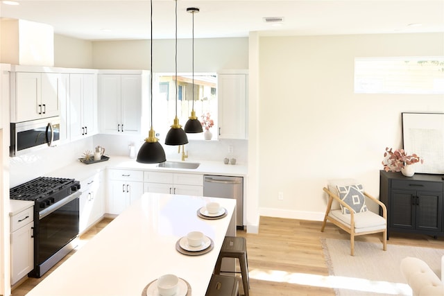 kitchen featuring pendant lighting, light wood-type flooring, white cabinetry, and stainless steel appliances