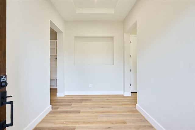 corridor with light hardwood / wood-style floors and a tray ceiling