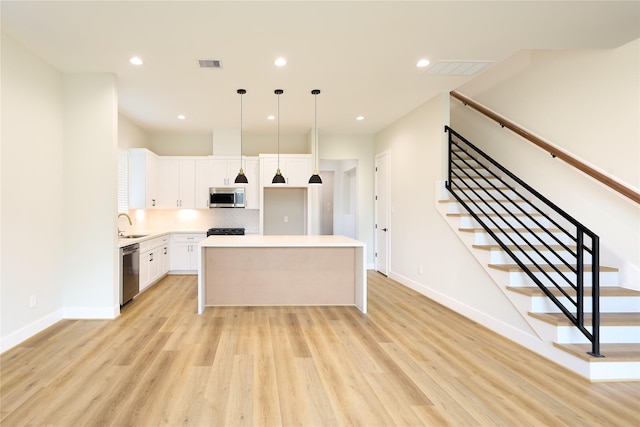 kitchen featuring a kitchen island, appliances with stainless steel finishes, white cabinets, hanging light fixtures, and light hardwood / wood-style floors