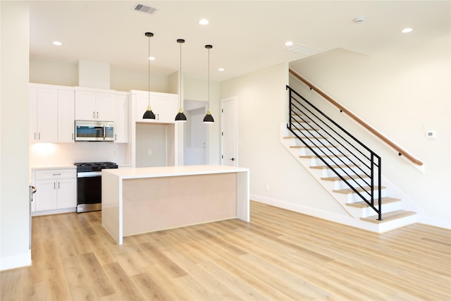 kitchen featuring white cabinetry, decorative light fixtures, a center island, light wood-type flooring, and appliances with stainless steel finishes